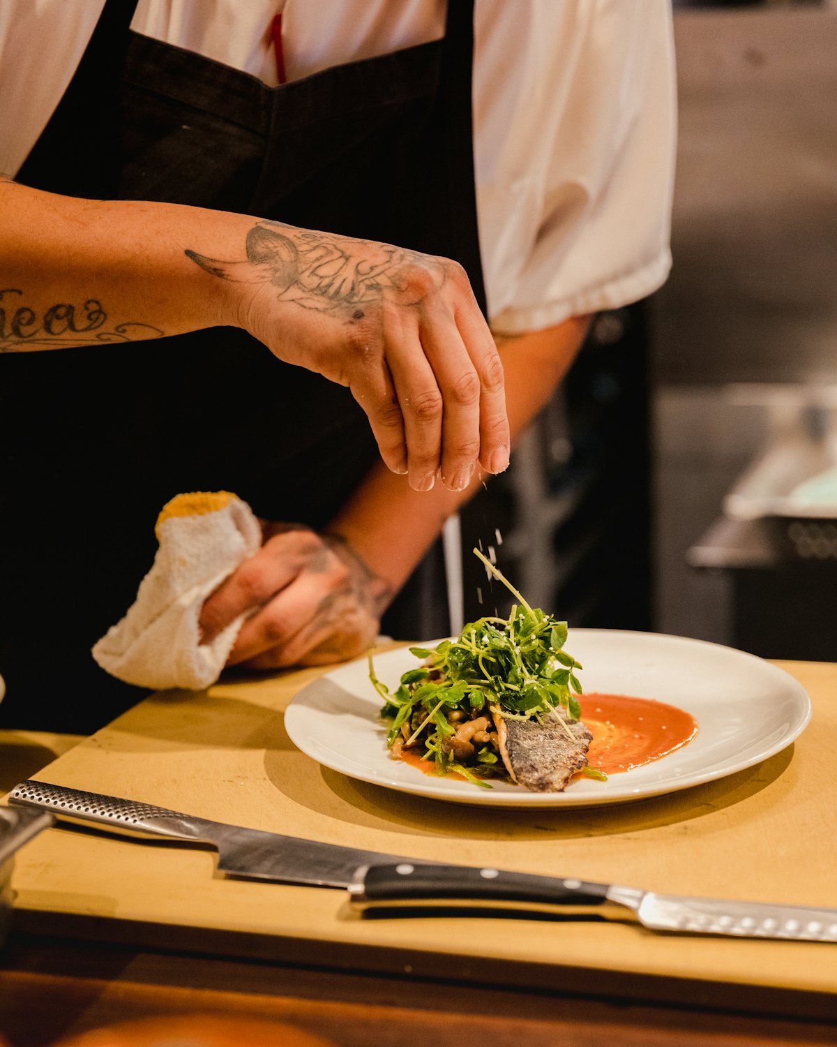 A cook's hands finishing a plated dish